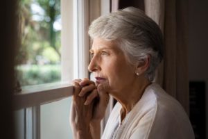 an elderly woman stares out the window having trouble going outside due to her anxiety