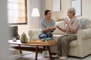 A nurse hands food to a senior on couch inside a memory care facility