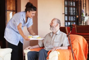 a nurse delivers lunch to a sitting senior adult who has had his length of respite care extended