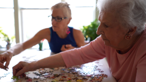 Two seniors put puzzle together while asking, "what is memory care for seniors?"