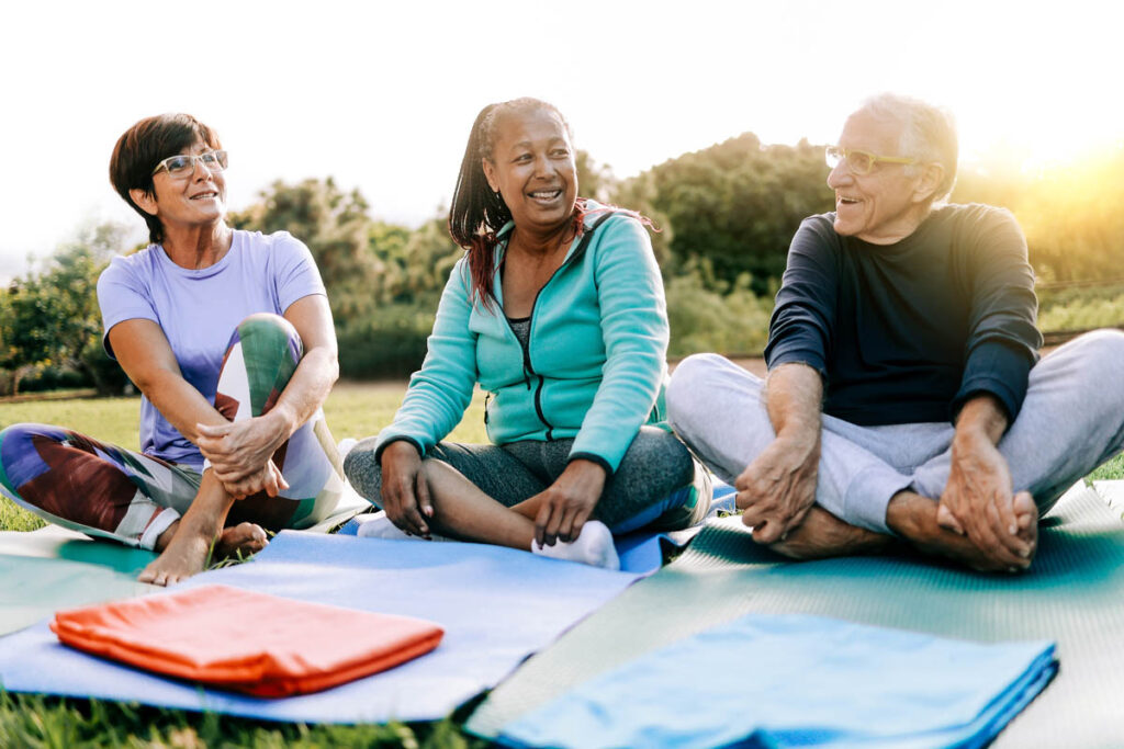 Seniors smile at one another while sitting in the grass as they enjoy social activities in senior living communities