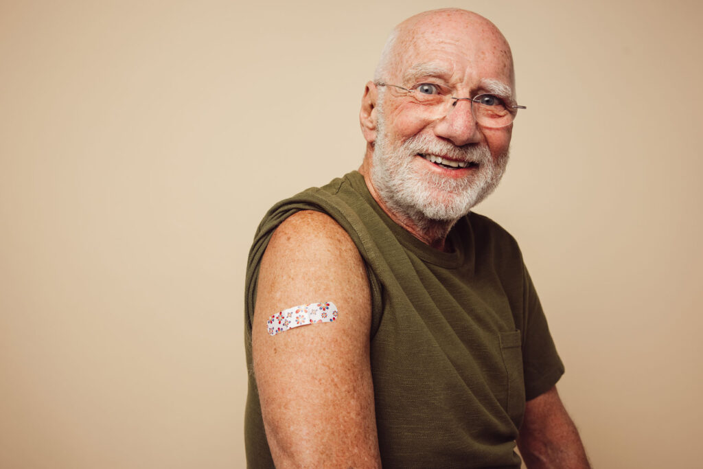 Man with bandaide smiles after discussing vaccines every senior should consider